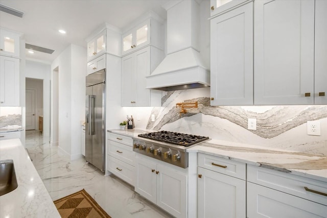 kitchen featuring white cabinetry, stainless steel appliances, light stone countertops, and custom range hood