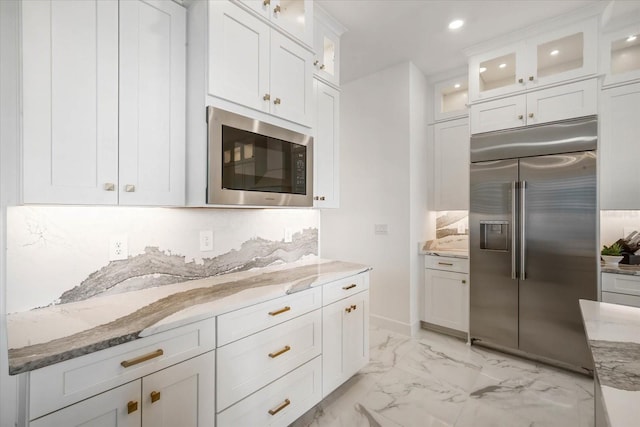 kitchen featuring white cabinetry, built in appliances, light stone counters, and backsplash