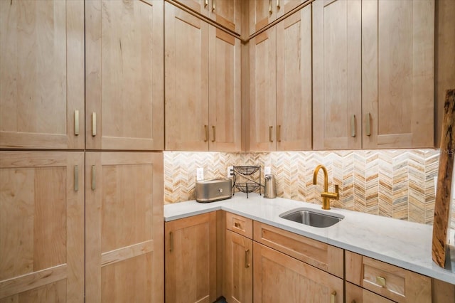 kitchen with light brown cabinetry, sink, backsplash, and light stone counters