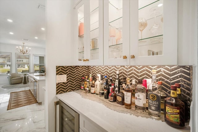 bar featuring white cabinetry, sink, beverage cooler, backsplash, and a notable chandelier