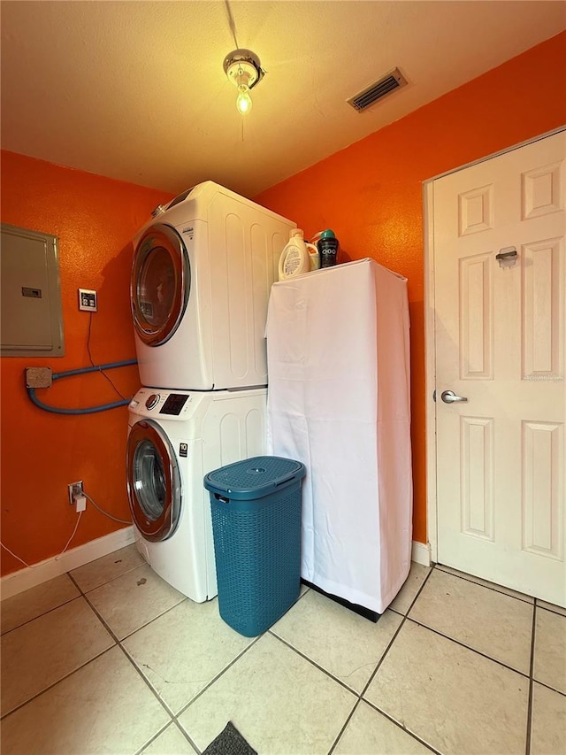 clothes washing area with stacked washer and dryer, electric panel, and light tile patterned floors