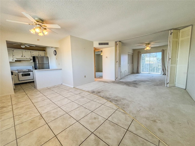 interior space featuring electric stove, stainless steel refrigerator, ceiling fan, a textured ceiling, and light colored carpet