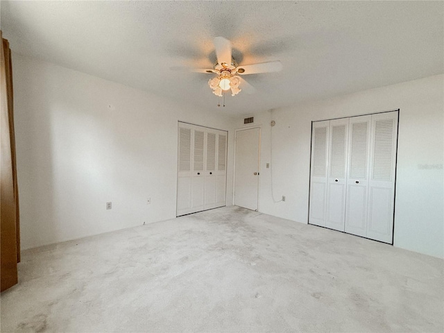 unfurnished bedroom featuring multiple closets, light colored carpet, and ceiling fan