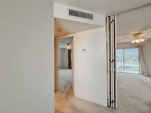 hall with light carpet and a textured ceiling