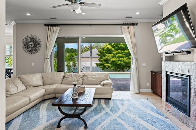 tiled living room featuring a tile fireplace, ornamental molding, ceiling fan, and a textured ceiling