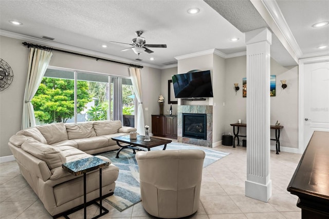 living room featuring crown molding, a textured ceiling, a tile fireplace, ceiling fan, and decorative columns