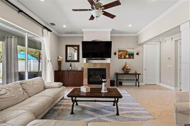 living room featuring a tiled fireplace, light tile patterned floors, crown molding, and ceiling fan