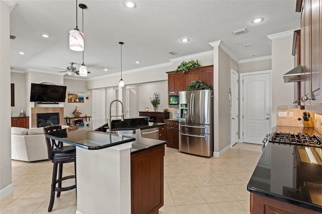 kitchen with sink, light tile patterned floors, appliances with stainless steel finishes, a fireplace, and a kitchen island with sink