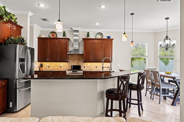 kitchen featuring a center island with sink, appliances with stainless steel finishes, pendant lighting, and wall chimney range hood