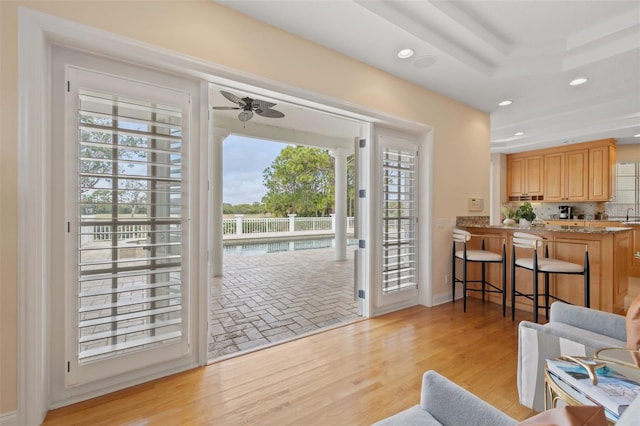 entryway with ceiling fan, sink, light wood-type flooring, and a tray ceiling