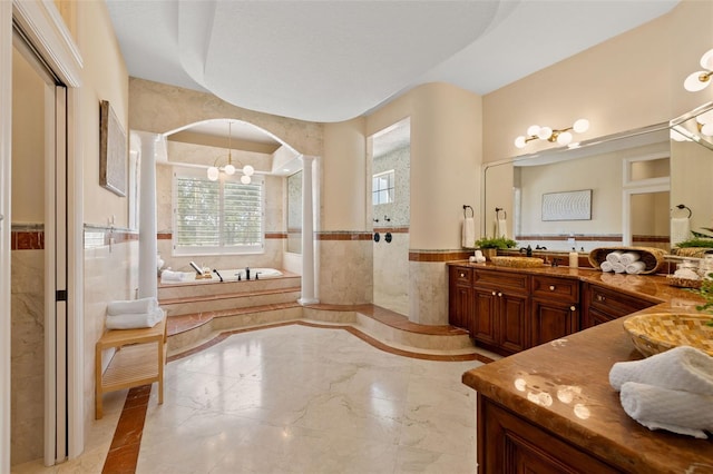 bathroom featuring independent shower and bath, vanity, tile walls, and a notable chandelier