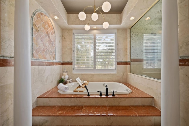 bathroom with a relaxing tiled tub, a raised ceiling, and tile walls