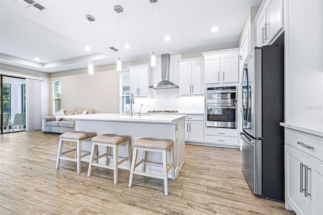 kitchen featuring appliances with stainless steel finishes, pendant lighting, white cabinets, and wall chimney exhaust hood