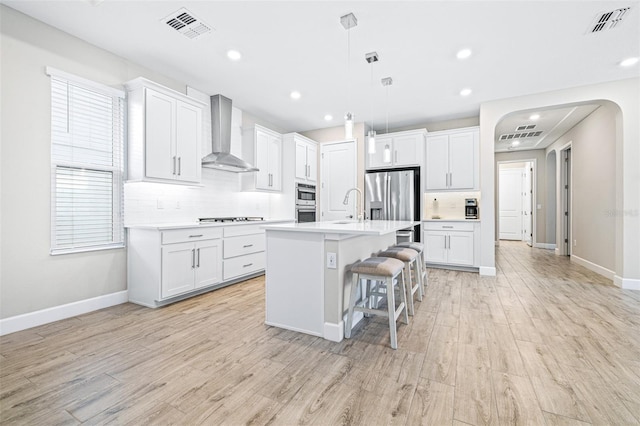 kitchen featuring white cabinetry, a center island with sink, and wall chimney range hood