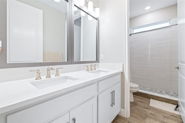 bathroom with wood-type flooring, toilet, vanity, and a tile shower