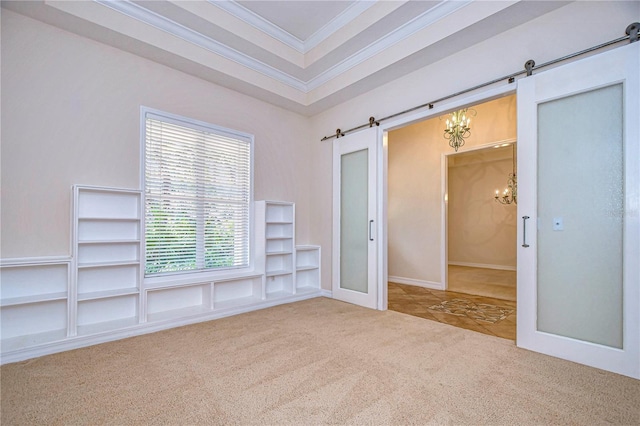 spare room featuring ornamental molding, a tray ceiling, a notable chandelier, a barn door, and carpet