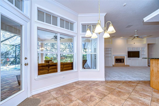 unfurnished dining area featuring crown molding, carpet, built in shelves, a textured ceiling, and ceiling fan with notable chandelier