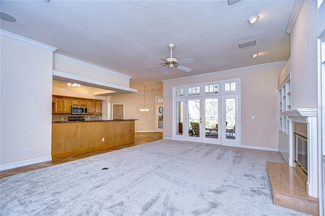 unfurnished living room with ceiling fan with notable chandelier, a fireplace, ornamental molding, light colored carpet, and a textured ceiling