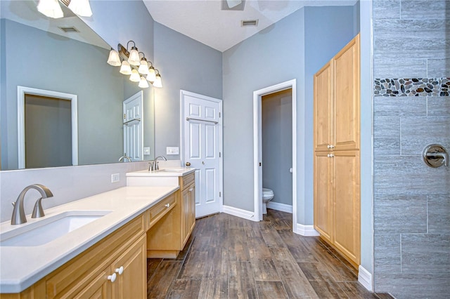 bathroom with toilet, a shower, wood-type flooring, vanity, and ceiling fan