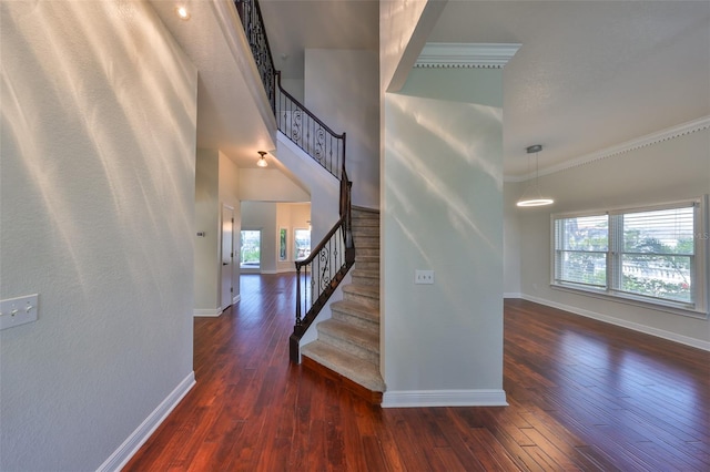 staircase featuring ornamental molding, wood-type flooring, a towering ceiling, and baseboards