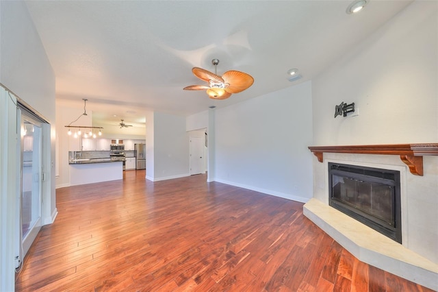 unfurnished living room with a glass covered fireplace, ceiling fan, baseboards, and wood finished floors