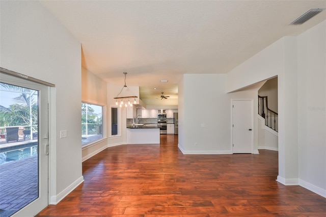 unfurnished living room with an inviting chandelier, stairs, visible vents, and dark wood finished floors