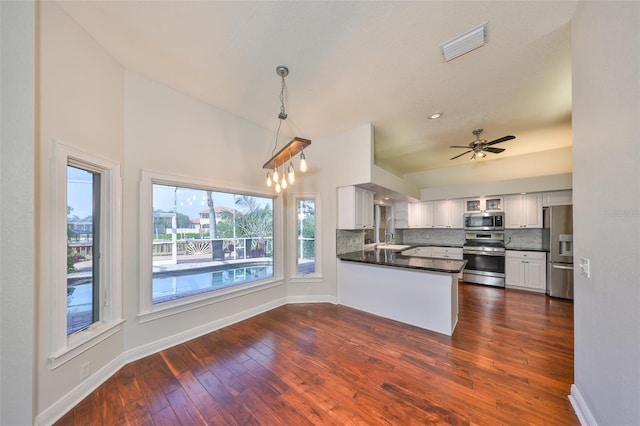 kitchen featuring stainless steel appliances, dark countertops, tasteful backsplash, visible vents, and a peninsula