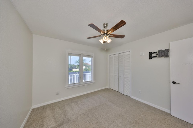 unfurnished bedroom with baseboards, light colored carpet, ceiling fan, a textured ceiling, and a closet