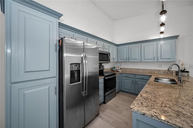 kitchen with sink, hanging light fixtures, light stone counters, stainless steel appliances, and light hardwood / wood-style flooring