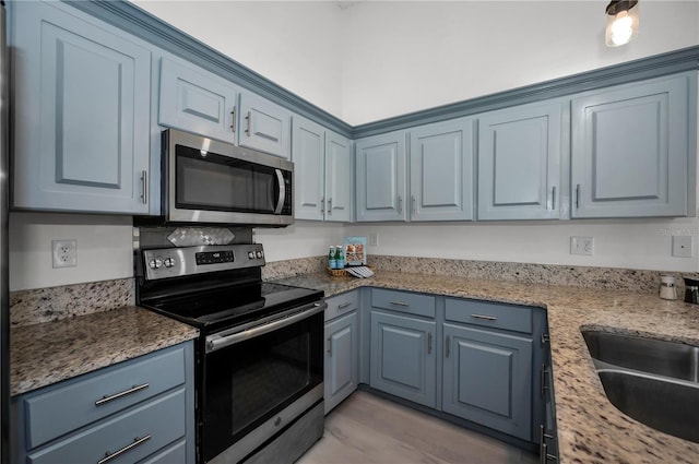 kitchen featuring appliances with stainless steel finishes, sink, light stone counters, blue cabinetry, and light wood-type flooring