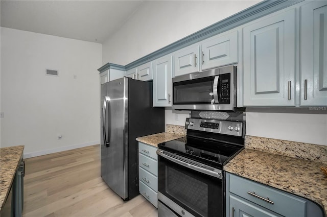 kitchen featuring appliances with stainless steel finishes, light hardwood / wood-style flooring, and dark stone counters