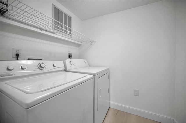 laundry area with a textured ceiling, light hardwood / wood-style floors, and washing machine and clothes dryer