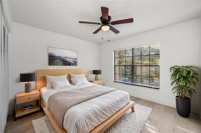 bedroom with ceiling fan, light hardwood / wood-style flooring, and a textured ceiling