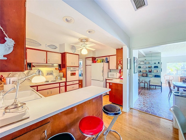 kitchen with sink, white appliances, light hardwood / wood-style flooring, ceiling fan, and kitchen peninsula