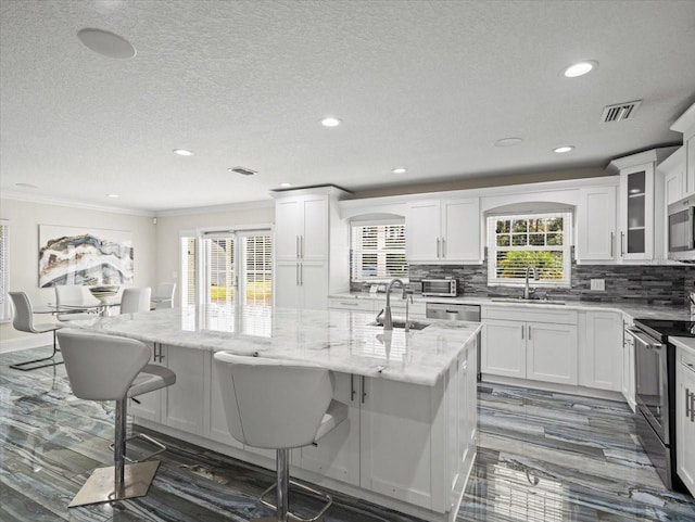 kitchen with sink, white cabinetry, stainless steel appliances, light stone countertops, and a kitchen island with sink