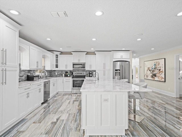 kitchen featuring appliances with stainless steel finishes, a center island, white cabinets, and light stone counters