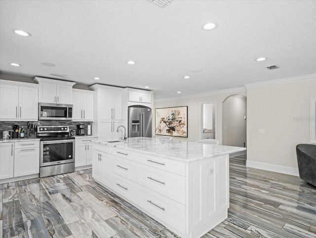 kitchen with light stone countertops, an island with sink, appliances with stainless steel finishes, and white cabinets