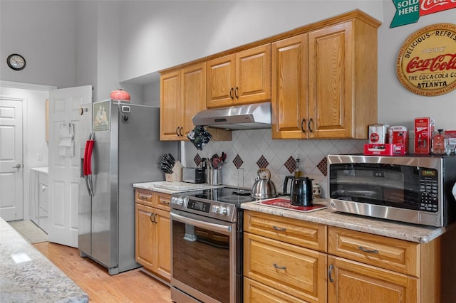 kitchen with light stone countertops, appliances with stainless steel finishes, light hardwood / wood-style floors, and decorative backsplash