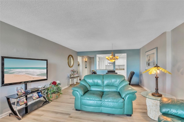 living room with an inviting chandelier, a textured ceiling, and light wood-type flooring