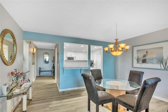 dining room with light hardwood / wood-style floors, a textured ceiling, and a notable chandelier