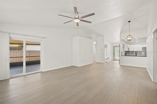 unfurnished living room featuring lofted ceiling, ceiling fan with notable chandelier, and light hardwood / wood-style flooring