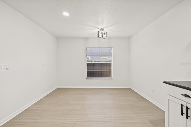 unfurnished dining area featuring a chandelier, a textured ceiling, and light wood-type flooring