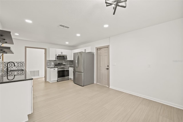 kitchen with backsplash, light hardwood / wood-style floors, white cabinets, and appliances with stainless steel finishes