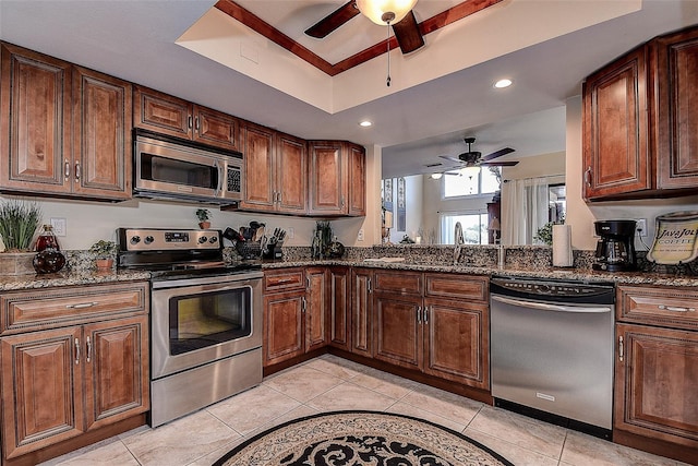 kitchen featuring appliances with stainless steel finishes, a tray ceiling, light tile patterned floors, and dark stone counters