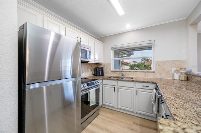 kitchen with appliances with stainless steel finishes, white cabinetry, sink, backsplash, and crown molding