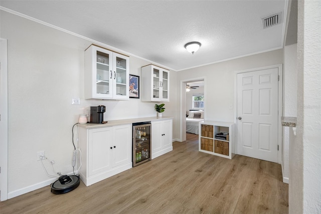 bar featuring wine cooler, white cabinetry, ornamental molding, and light wood-type flooring