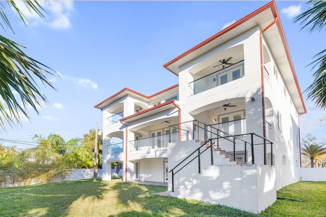 back of house featuring ceiling fan, a balcony, and a lawn