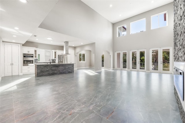 unfurnished living room with recessed lighting, a sink, a towering ceiling, and baseboards