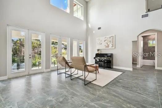 sitting room featuring french doors, a towering ceiling, and concrete flooring