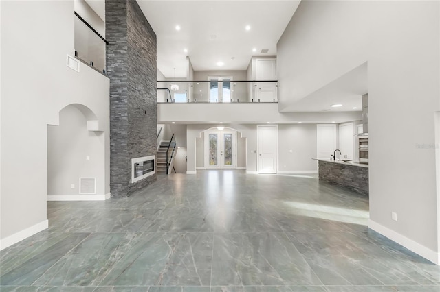 unfurnished living room featuring a stone fireplace, a towering ceiling, sink, and french doors